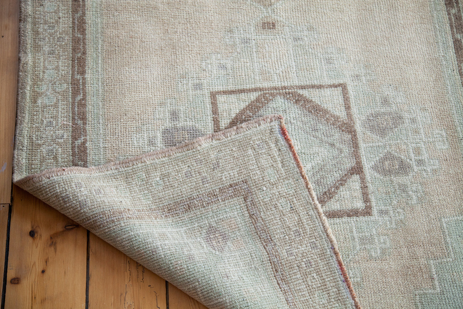 Folded Vintage Oushak rug showing pale mint geometric pattern and hand-knotted foundation.